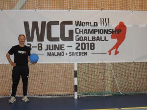 Alexander Knecht mit einem Goalball in der Hand vor dem Banner für die Goalball WM in Malmö (Schweden)